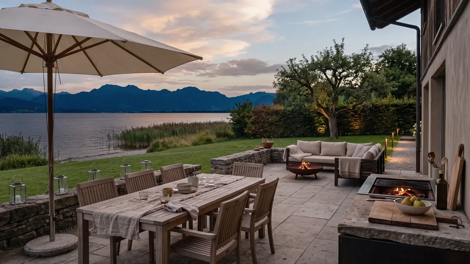 Terrasse in der Abenddämmerung mit Gartenmöbeln, Sonnenschirm, Außenküche und Licht