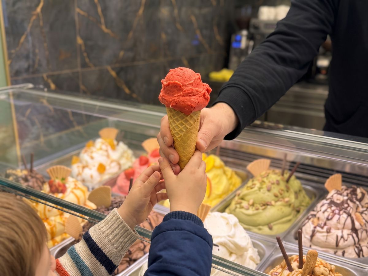 Eine Hand reicht eine Eiswaffel über die Theke an zwei Kinderhände