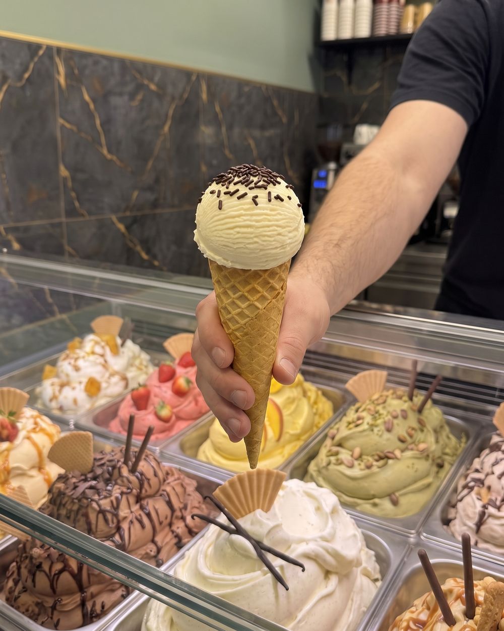 Hand reicht eine Waffel mit Vanilleeis und Schokostreuseln über die Theke