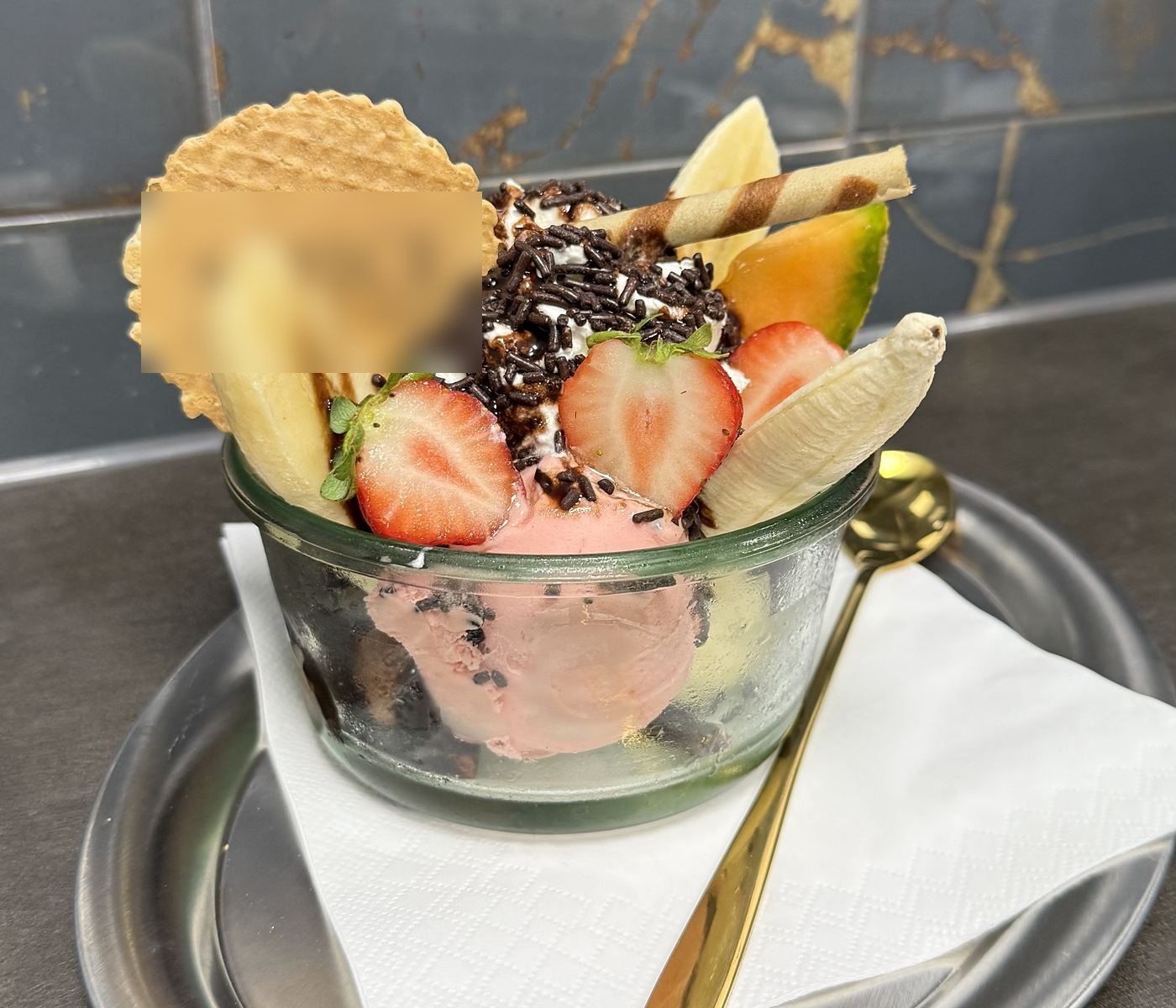 Fruchtbecher mit Erdbeeren und Mustermann-Waffel vor der Marmorwand mit Goldadern