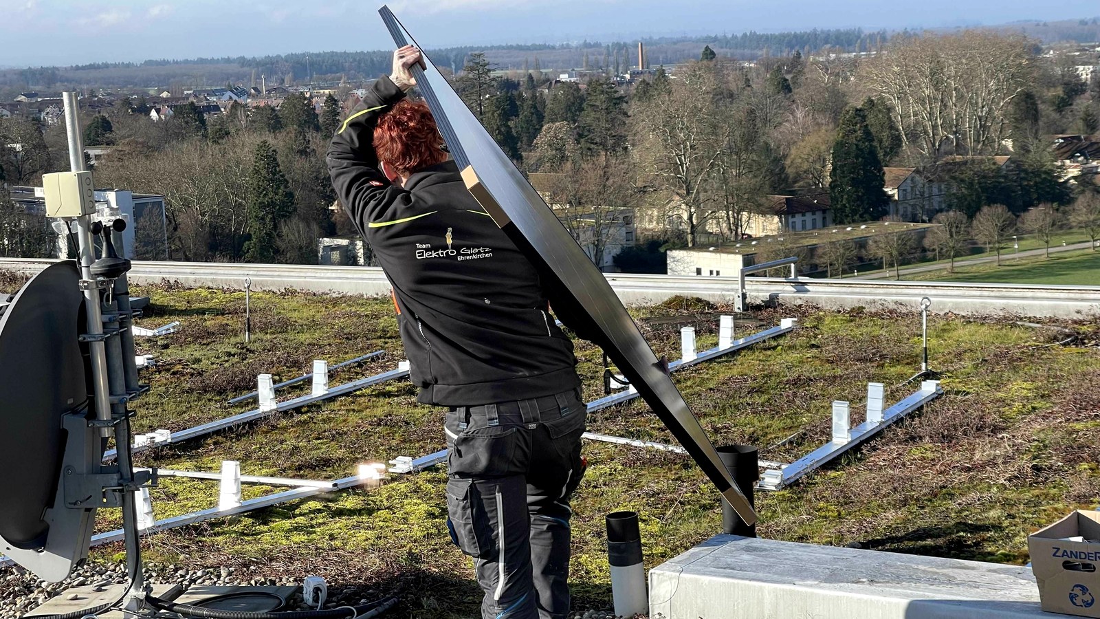 Monteur von Elektro Mustermann auf einem Dach beim Aufstellen eines Moduls
